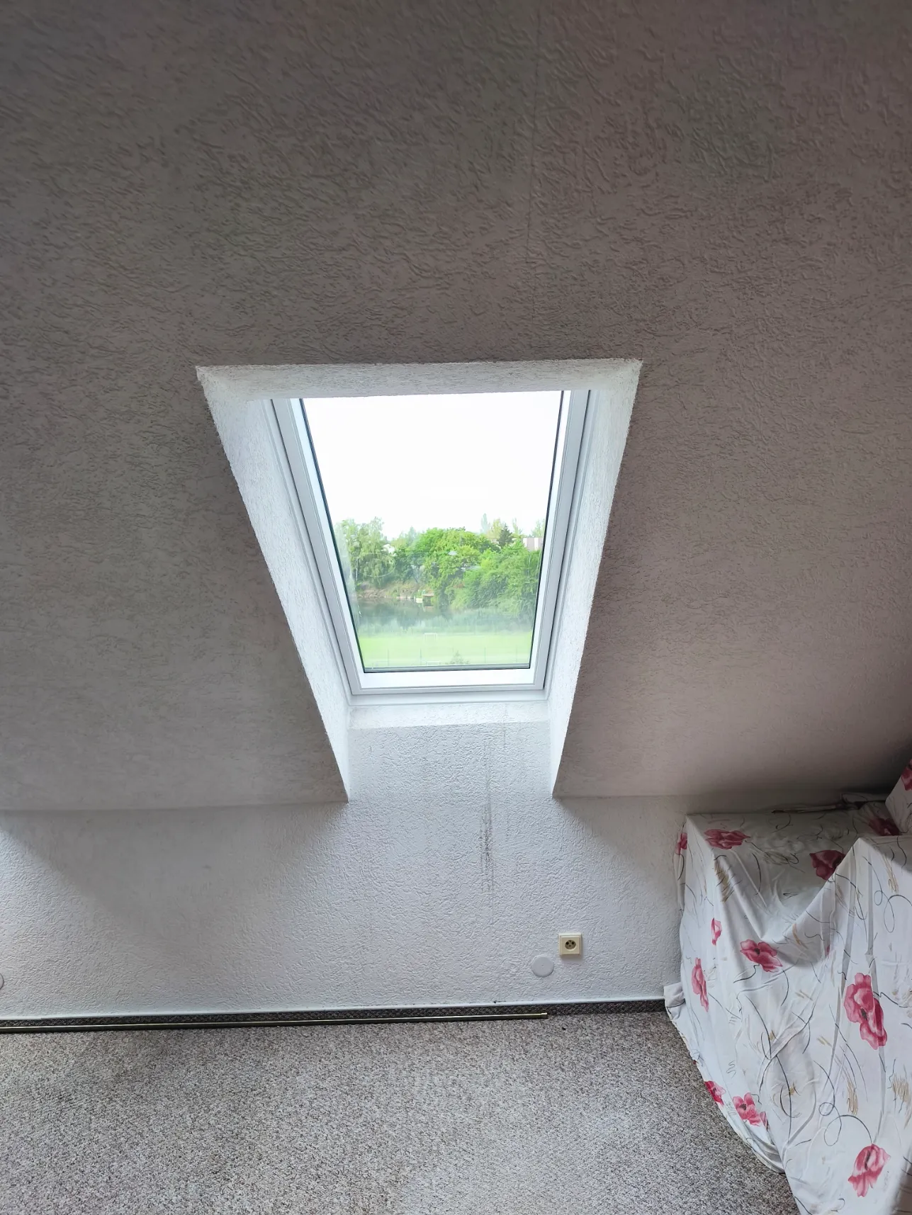 Střešní okno v šedé šikmé stěně nad radiátorem
