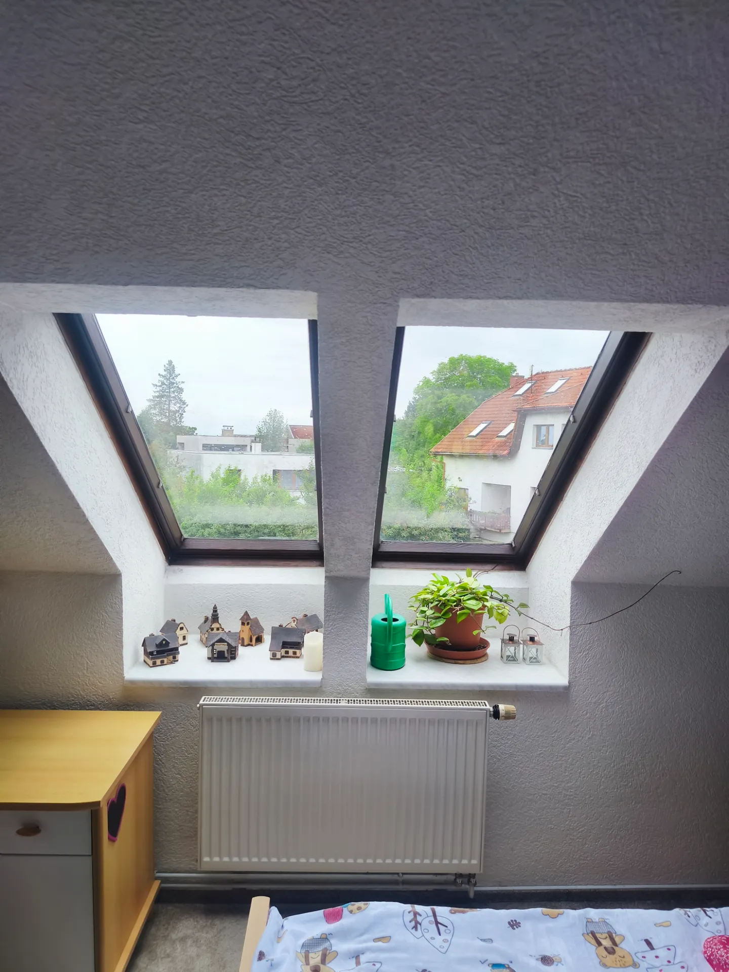 Dvojice střešních oken s květinami na parapetu nad radiátorem