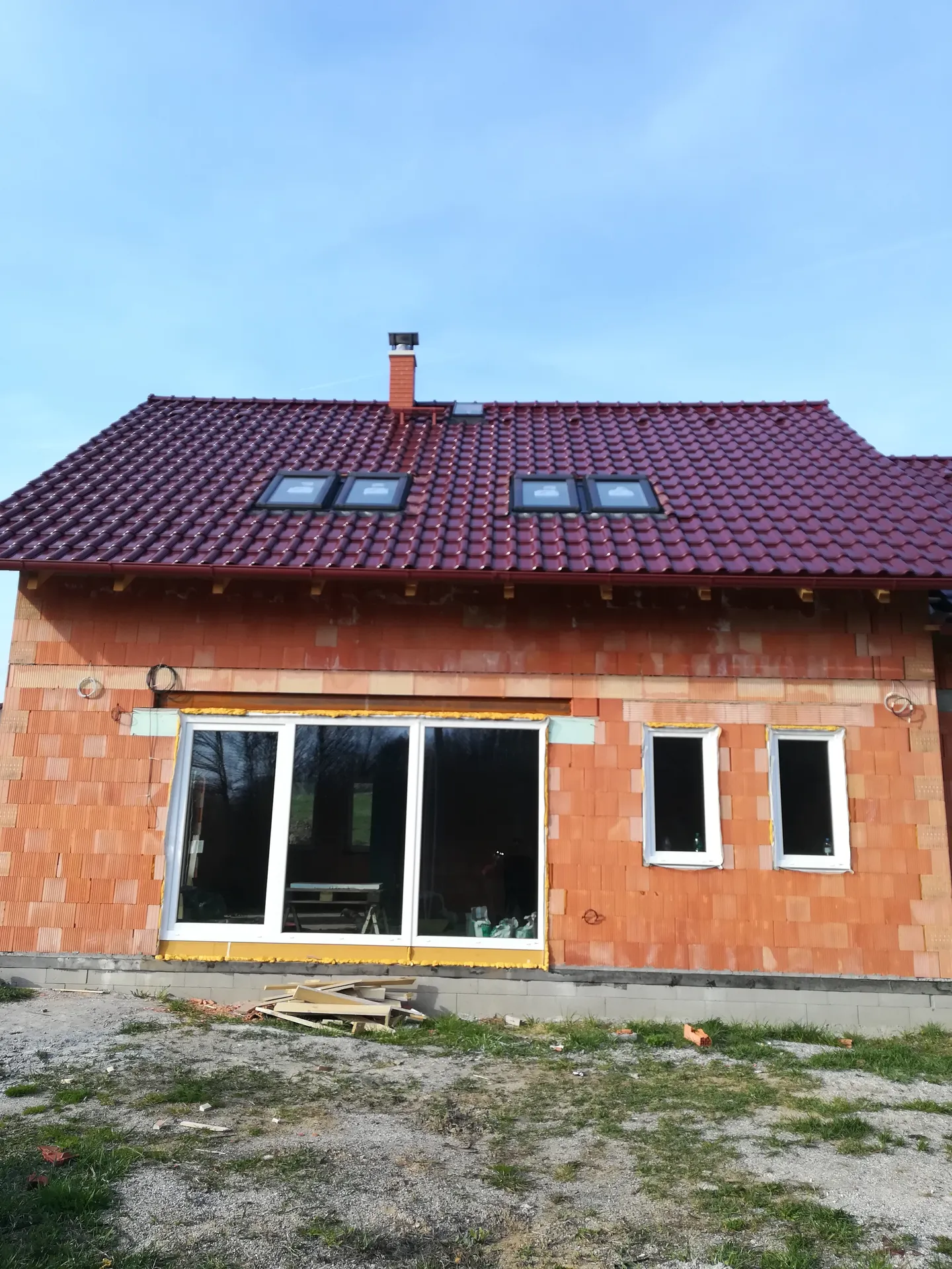 Rozestavěný cihlový dům s červenou střechou a čtyřmi střešními okny