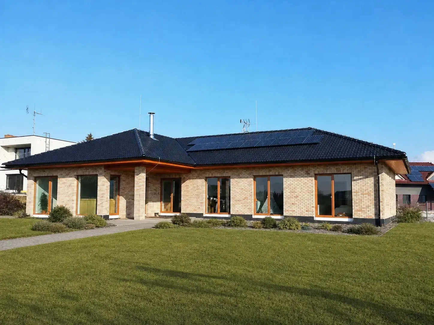 Přízemní rodinný dům s černou valbovou střechou a solárními panely