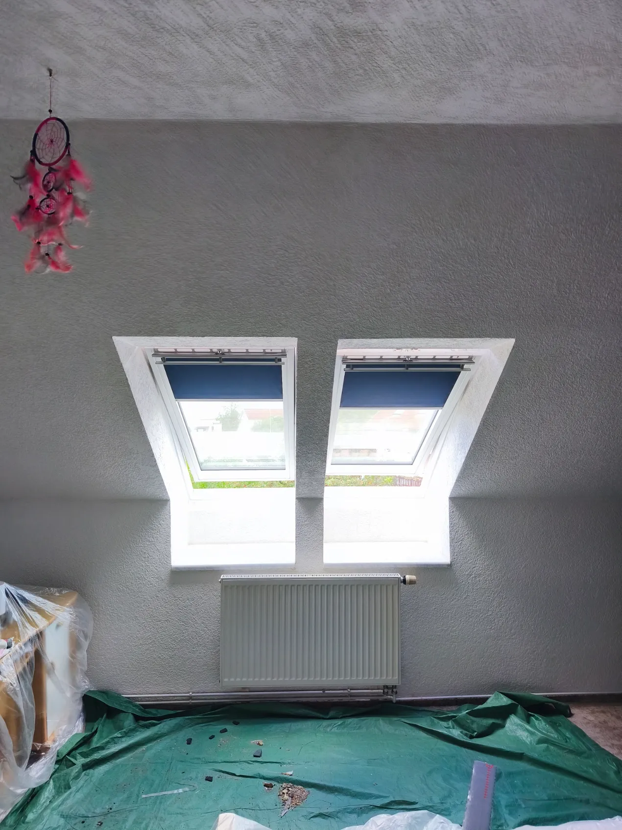 Dvě střešní okna v šedé šikmé stěně nad radiátorem